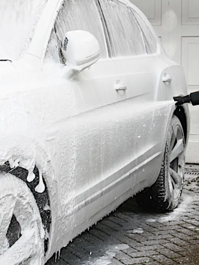 A car under a full coat of snow foam being rinsed on a cobbled street in Highbury