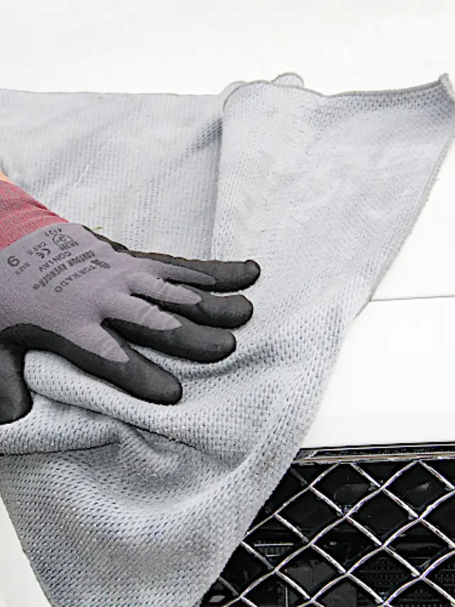 A gloved hand buffing a car panel dry with a microfibre cloth in Wimbledon