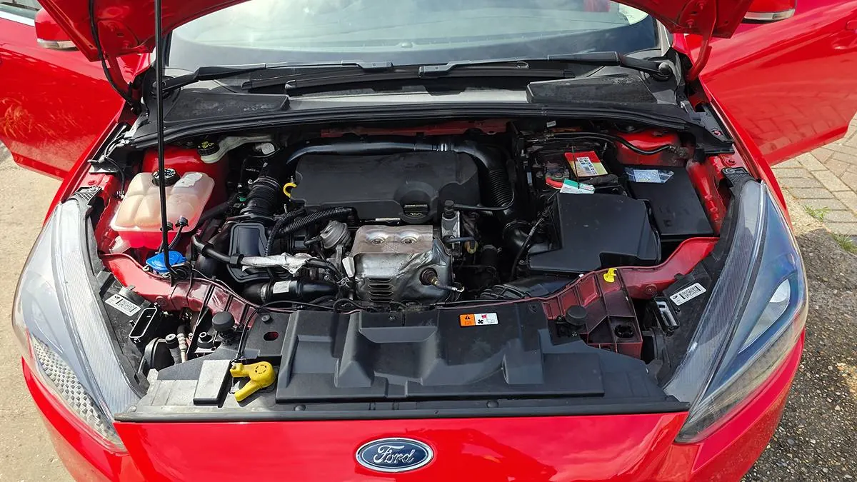 Engine bay of a red Ford Focus with the bonnet open on the driveway
