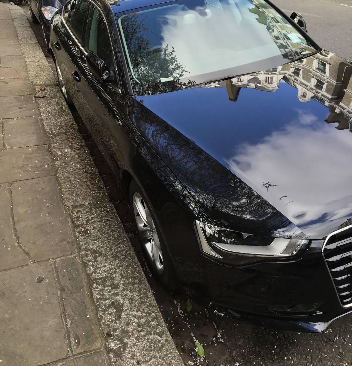 A black bonnet with a mirror finish reflecting the sky after washing and waxing
