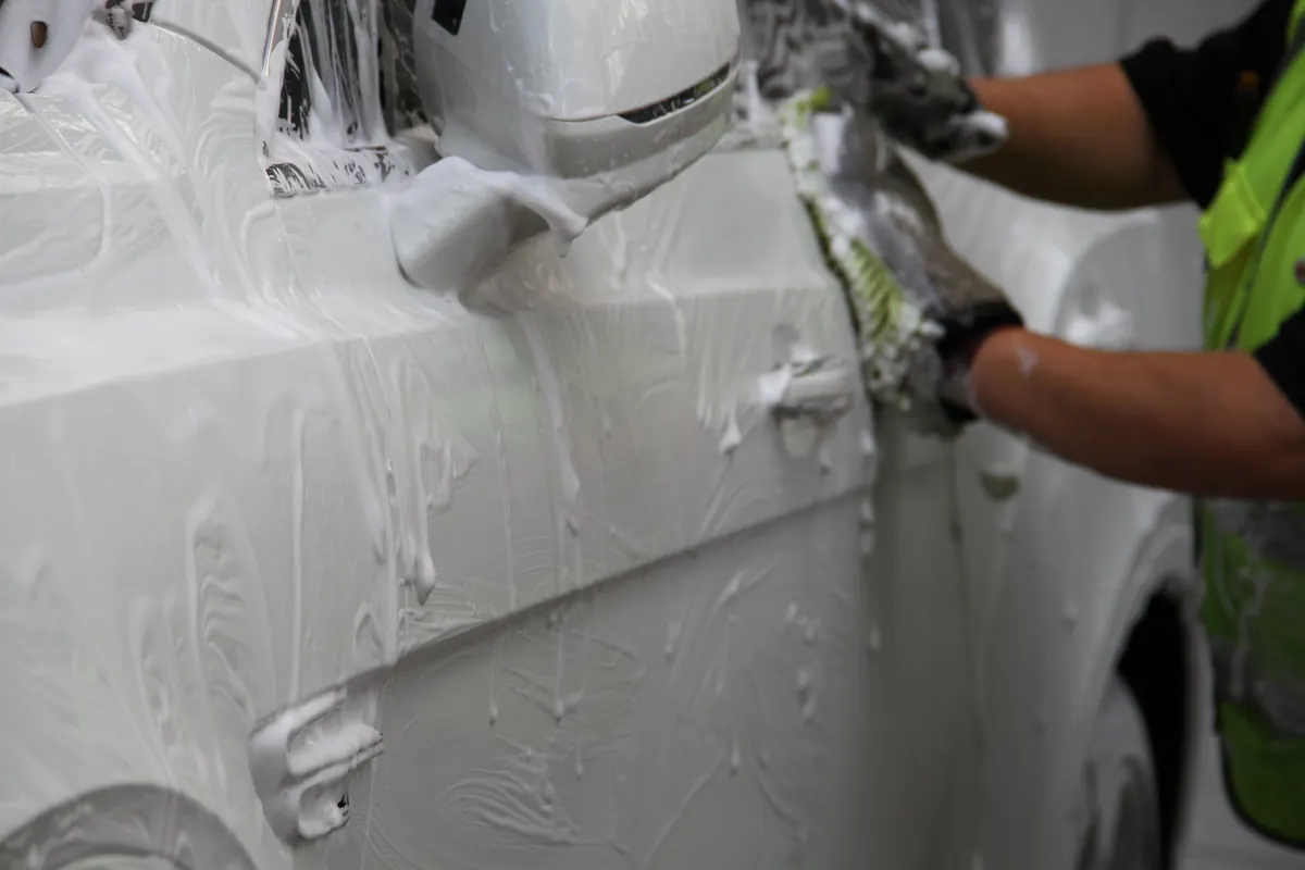 A gloved hand with a wash mitt hand washing a foamed white car door