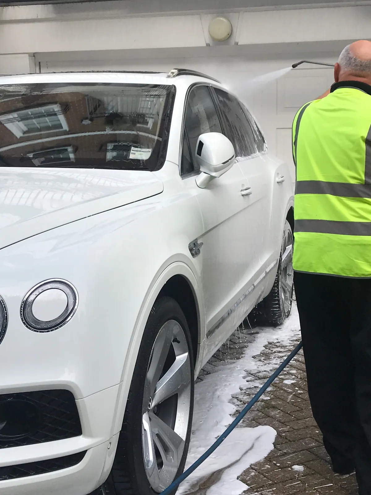 A valeter in hi-vis rinsing a white SUV on a driveway