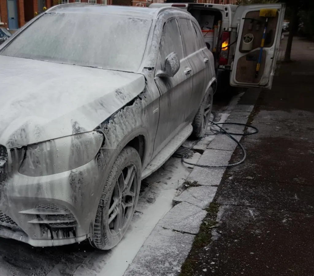 A Mercedes SUV covered in pre-wash snow foam at the kerb